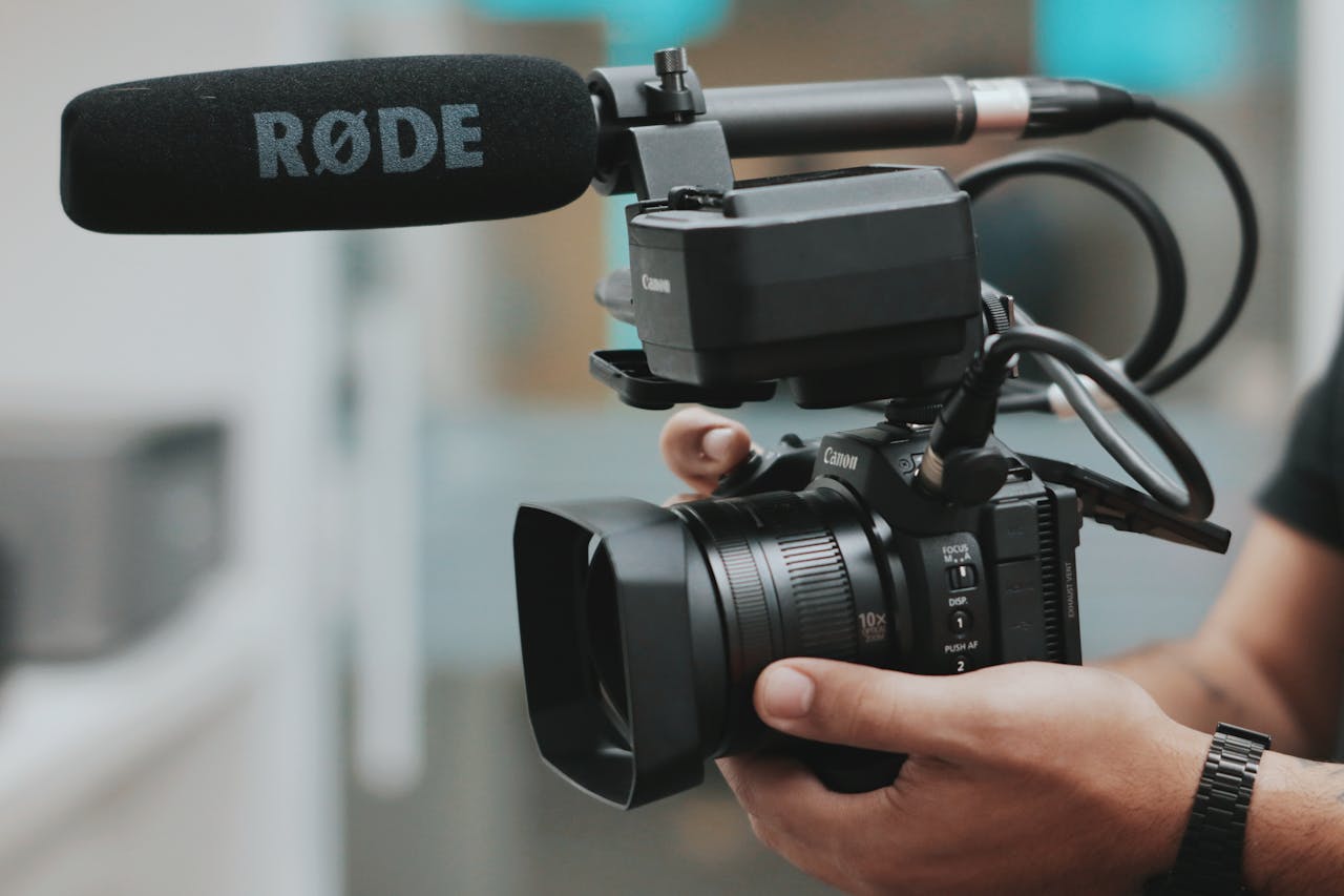 Home Close-up of hands holding a professional video camera with a RØDE microphone attached.